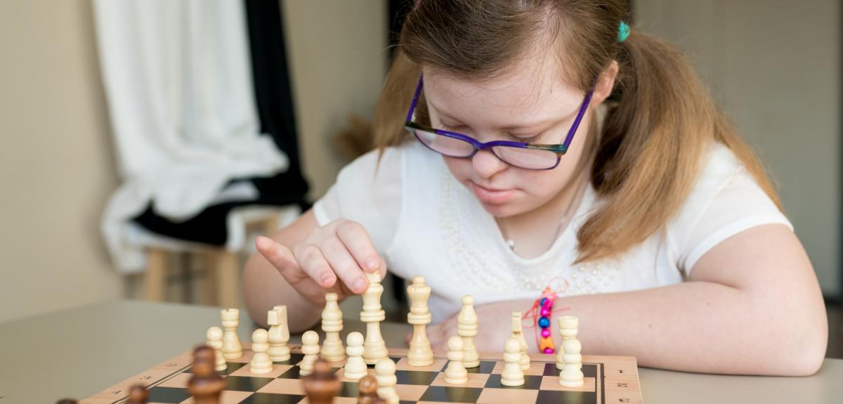 Teenager girl with Down syndrome playing chess on the game board